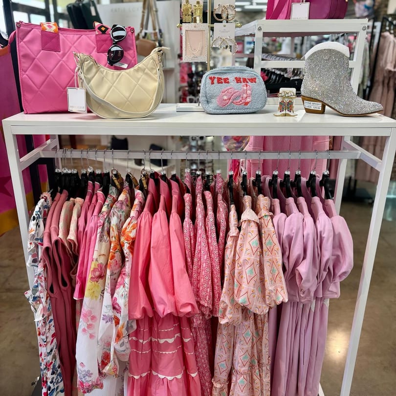 A boutique display with pink clothing, handbags, jewelry, and a sparkly cowboy boot.
