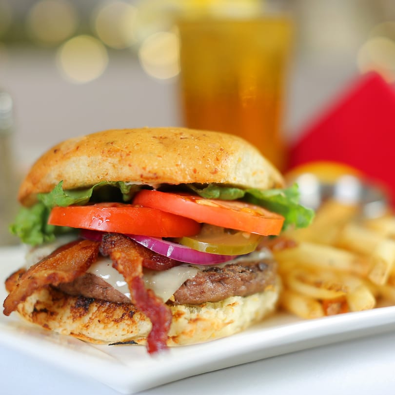A bacon cheeseburger with lettuce, tomato, onion, and pickles, served with fries and a drink.