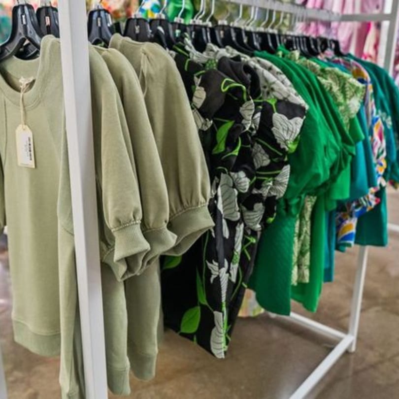 A clothing rack displays various green and patterned tops, some with price tags, in a retail setting.
