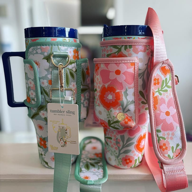 Two floral-patterned tumbler slings, one mint green and one pink, with adjustable straps and pockets.