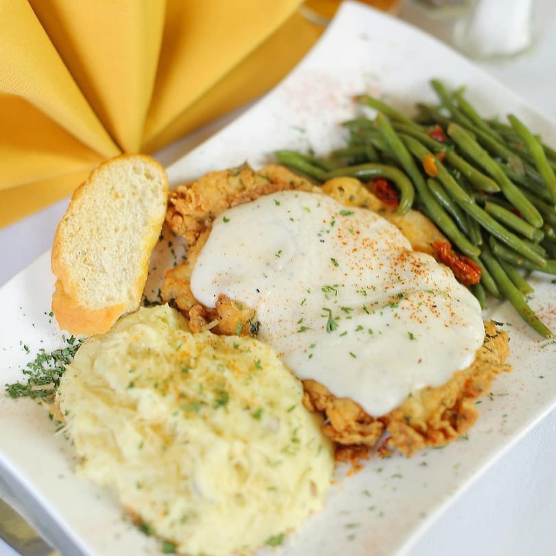 Chicken fried steak with gravy, mashed potatoes, green beans, and a slice of bread.