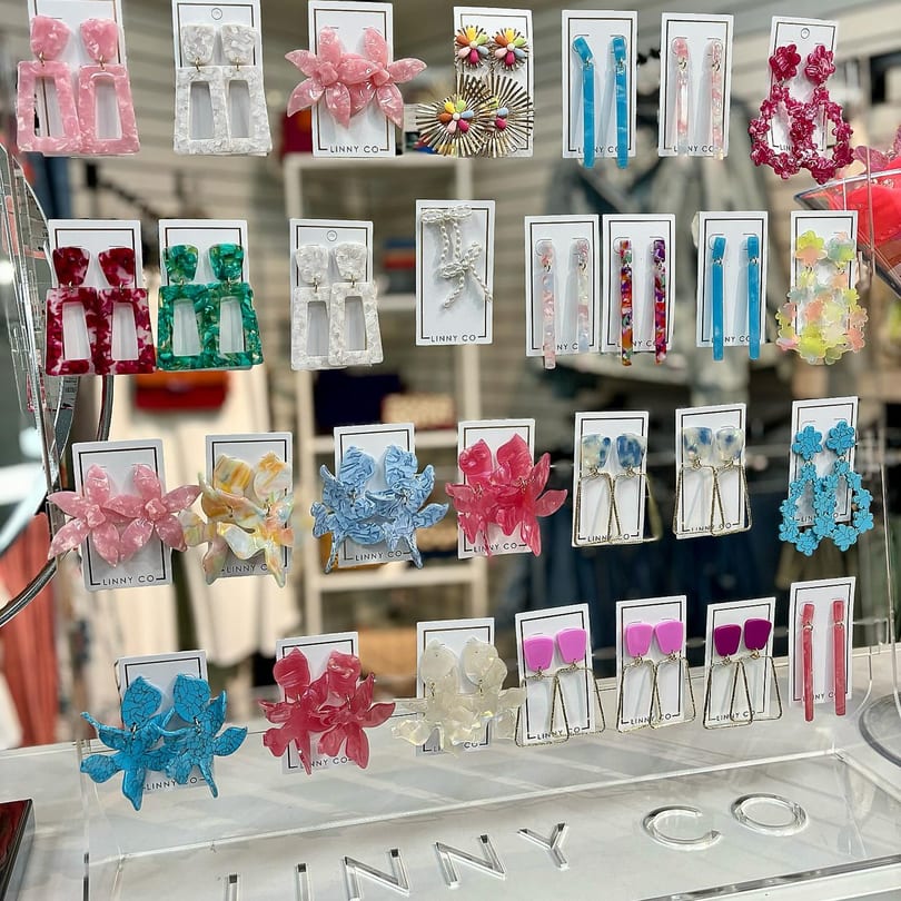 A display of colorful earrings in various shapes and sizes, including floral and geometric designs.