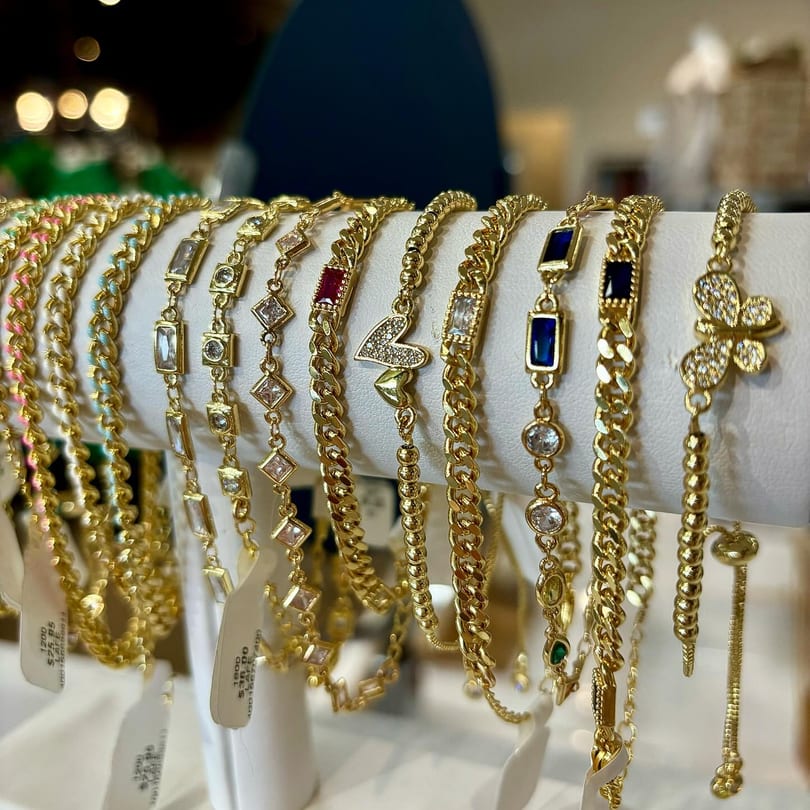 A display of various gold bracelets with colorful gems and charms, some with price tags.