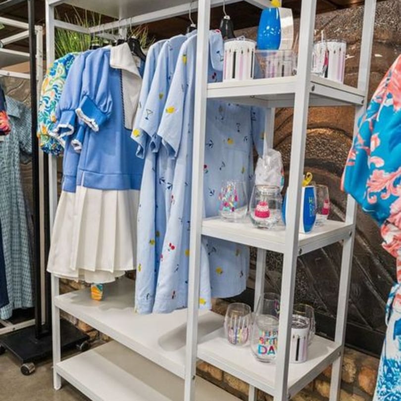 A white shelving unit displays blue and white clothing, along with various decorative glasses and bottles.